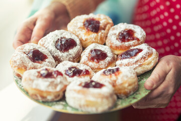 Plate full of jam-filled donuts with sugar coating held in the hands of an older woman