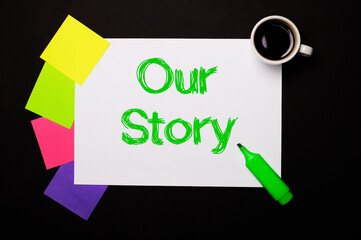 A sheet of paper with the OUR STORY, a cup of coffee, bright multi-colored stickers for notes and a green marker on a black background. View from above.