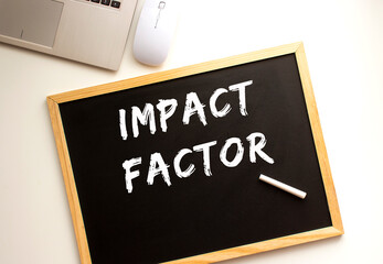 Text IMPACT FACTOR written in chalk on a slate board. Office desk.