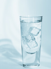 Glass of clean mineral sparkling water with ice on light blue background