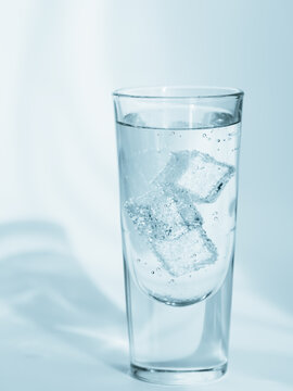 Glass of clean mineral sparkling water with ice on light blue background
