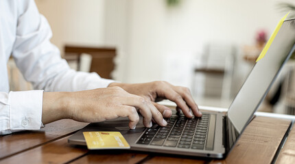 A man holds a credit card and uses a laptop. He is filling out credit card information for online shopping, credit cards can be used to pay for goods and services through physical stores and online.