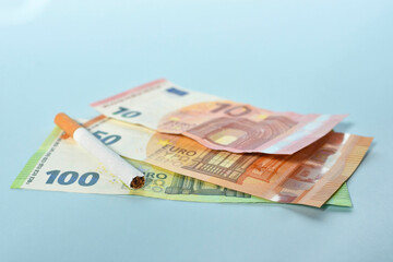 Cigarettes and money on blue background. Euro banknotes and coins, cost of smoking, cigarette price concept. Selective focus