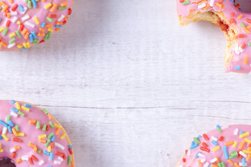 Delicious donuts with pink icing, strawberry jelly filling and colorful sprinkles on wooden background with copy space. Sweet American pastry for a birthday party or other celebrations. Pastel colors.