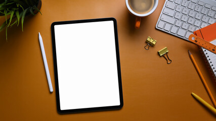 Mock up digital tablet with empty screen, stationery, keyboard and stylus pen on orange background.