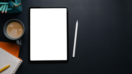 Mock up digital tablet with blank screen, coffee cup, stylus pen, notebook and copy space on black leather.