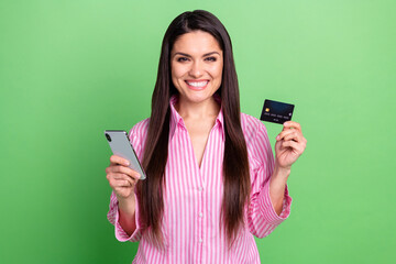 Portrait of attractive trendy cheerful girl holding in hands device card web order shopping isolated over green pastel color background