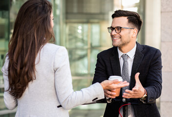 Two business people walking outside in front of modern business building.