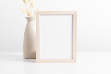 Beige frame mockup with dried flowers lagurus in beige vase on white table. Front view. Place for...