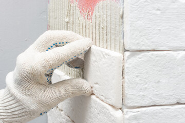 Tiler hands in the process of laying white rectangular tiles on a wall in an apartment of a residential building. Construction and renovation of a modern house.