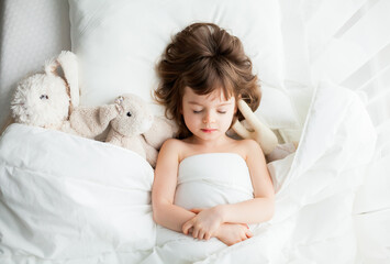 Adorable little girl sleeping in white bed with rabbit toys