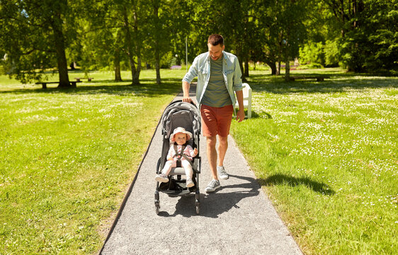 family, fatherhood and people concept - happy father with child in stroller walking at summer park