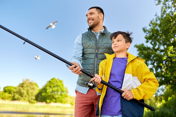 family, generation, summer holidays and people concept - happy smiling father and son with fishing rods on river berth
