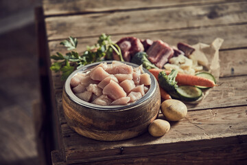 Meat in dog bowl near assorted vegetables on table