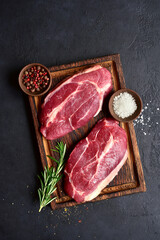 Raw organic marbled beef steaks with spices  on a wooden cutting board . Top view with copy space.