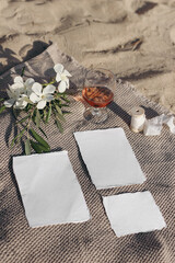 Summer wedding stationery mockups set. Vacation still life. Picnic on golden Mediterranean beach sand. Glass of red wine, white oleander flowers and olive branches on beige towel. Top view, vertical.