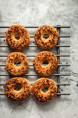 Baked round peanut cookies sprinkled with chopped peanuts on a cooling rack, marble backdrop. Top view vertical photo.