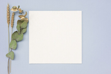 Square invitation card mockup with a gold eucalyptus branch. Top view of a white card mockup with branch of eucalyptus and dried golden ears