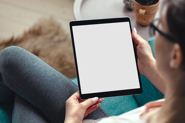 Young woman using digital tablet while sitting in a comfortable amchair at home, mock up