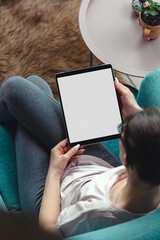 Young woman using digital tablet while sitting in a comfortable amchair at home, mock up