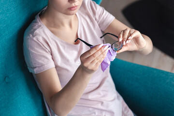 Young woman cleaning eyeglasses with a napkin while sitting in a chair