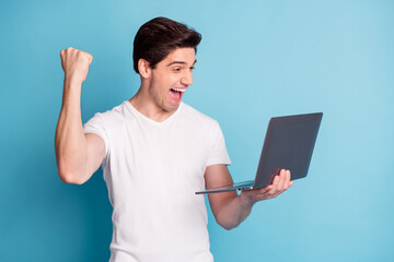 Portrait of astonished man arm hold laptop fist up open mouth scream yeah isolated on blue color background