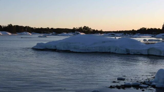 Sunset view of a winter landscape out in the Swedish archipelago. Rock cliffs and land covered in snow. Calm water and beautiful scenery with no people around. Footage made outside Oskarshamn, Sweden.