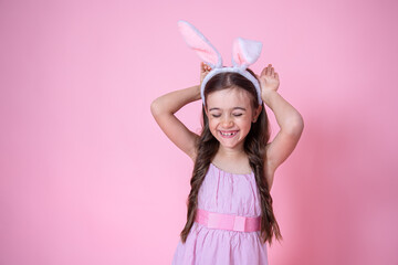 Beautiful little girl dressed in easter bunny ears and in a dress on a pink background.