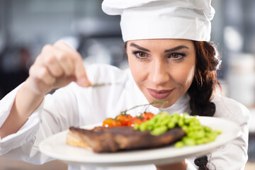 Professional female chef in a hat makes final touches on a freshly made steak before serving