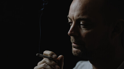 Close up of a young man smoking a cigarette looking thoughtful and stressed. Isolated on black background. Shallow depth of field.