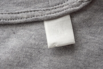 Blank white laundry care clothes label on gray fabric texture background