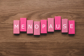 A pink wooden block with a text of menopause on wooden background.