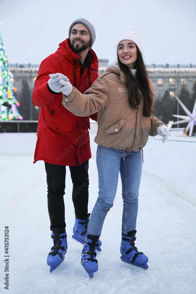 Wall mural Happy young couple skating at outdoor ice rink