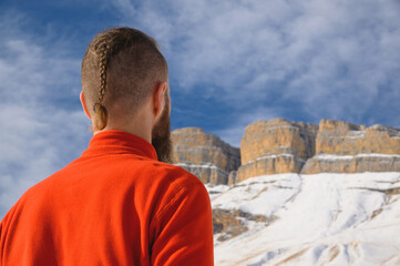 A bearded man with a brutal haircut in a red sweater looks at the epic not criminal rocks on a sunny day. The concept of overcoming difficulties