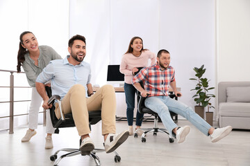 Happy office employees riding chairs at workplace