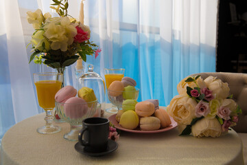 cupcakes of different colors in a pink plate next to a lush bouquet of flowers two glasses of yellow juice on the table