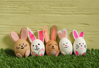 Easter eggs as cute bunnies on green grass against yellow wooden background