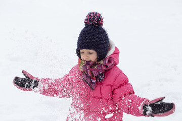 Warmly dressed little girl playing with snow close up.