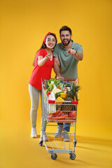 Young couple with shopping cart full of groceries on yellow background © New Africa