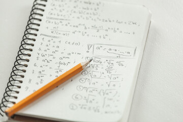 Math formulas are written in pencil on a piece of paper, math problems