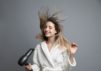Beautiful young woman using hair dryer on grey background