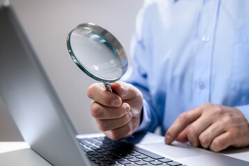 Businessman with magnifying glass reading online documents on laptop