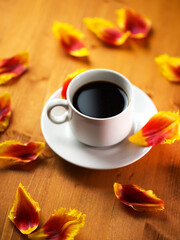 A cup of coffee in the spring morning, a wooden table covered with tulip flower petals