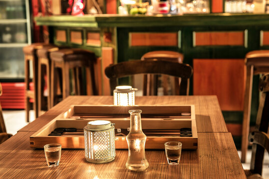 Greek cafe concepts, 2 small glasses with raki drink and carafe, tavli (Backgammon) at the blurred background. 