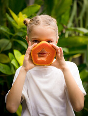 Charming little girl with fresh papaya. Caucasian girl holding slice of papaya fruit in front of...