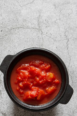 Chopped tomatoes cooked in a cast iron pot.  On a concrete background