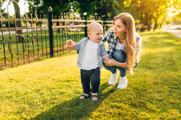 Fototapeta premium Mother helps her child learn the first step on the lawn