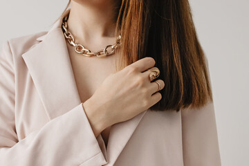 Woman in light beige jacket wearing golden chain necklace.