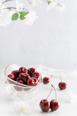 Cerezas en recipiente de vidrio sobre fondo blanco con rama de cerezo en flor