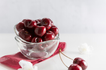 Cerezas en recipiente de vidrio sobre fondo blanco con rama de cerezo en flor